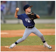 Imagem: Fotografia. Um menino usando chapéu, camisa e calça, segurando uma bola de beisebol com a mão esquerda e uma luva com a mão direita. Ele está com as pernas afastadas e o braço esquerdo flexionado para trás.  Fim da imagem.