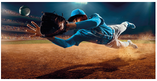 Imagem: Fotografia. Um homem usando boné e roupas azuis. Ele está inclinado para a lateral esquerda, segurando uma luva na direção de uma bola de beisebol. Fim da imagem.