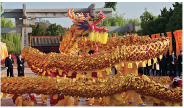 Imagem: Fotografia. Uma alegoria de um dragão dourado com pessoas em baixo.  Fim da imagem.
