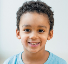 Imagem: Fotografia. Um menino com cabelo encaracolado e curto e olhos escuros está sorrindo. Fim da imagem.