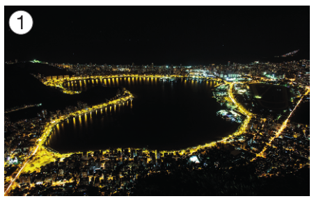 Imagem: Fotografia 1. Vista aérea de um lago escuro com luzes em volta. No entorno há construções com as luzes acesas. Fim da imagem.