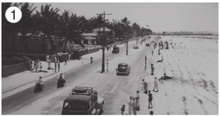 Imagem: Fotografia 1 em preto e branco. No centro há uma fileira de carros e nas laterais, pessoas andando. À esquerda há várias árvores e casas. Fim da imagem.