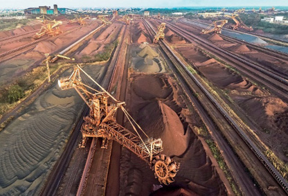 Imagem: Fotografia. Máquinas grandes entre morros de terra.  Fim da imagem.