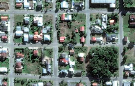 Imagem: Fotografia. Vista de cima de um bairro com construções, ruas e árvores. Fim da imagem.