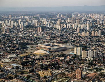 Imagem: Fotografia. Vista aérea de uma cidade com vários prédios, casas, ruas e árvores. Fim da imagem.