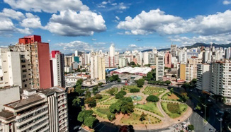 Imagem: Fotografia. No centro há um parque com árvores e em volta, muitos prédios, construções e ruas. Fim da imagem.