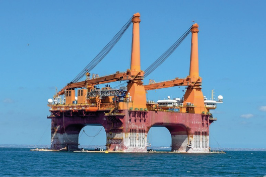 Imagem: Fotografia. Uma plataforma grande com duas torres altas sobre o mar. Fim da imagem.