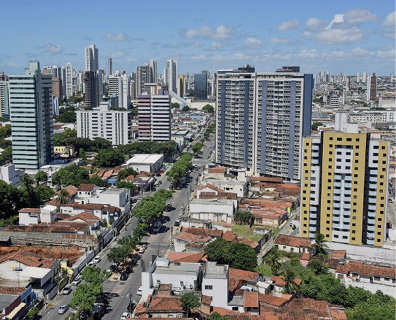 Imagem: Fotografia. Vista aérea de uma rua com árvores no centro. Nas laterais há várias casas e prédios. Fim da imagem.