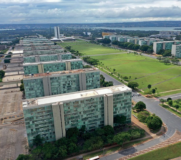 Imagem: Fotografia. Vista aérea de prédios retangulares. Ao lado há praças com árvores e ao fundo, mais prédios. Fim da imagem.