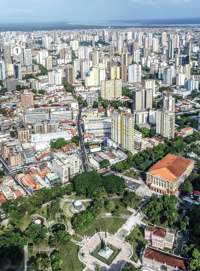 Imagem: Fotografia 1. Vista aérea de uma praça com árvores. Em volta há ruas, prédios e casas.  Fim da imagem.