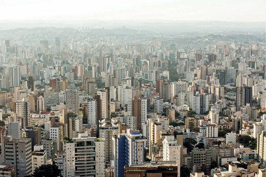 Imagem: Fotografia. Vista aérea de uma cidade com vários prédios e construções.   Fim da imagem.