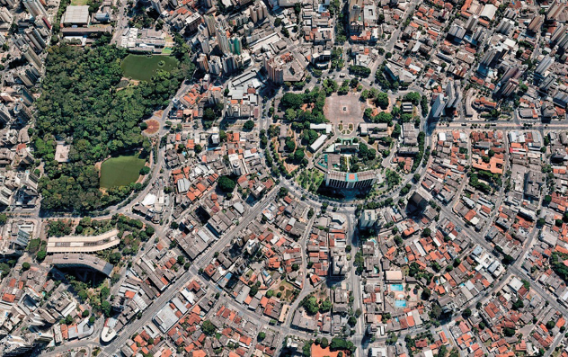 Imagem: Fotografia. Vista de cima de uma praça circular. Em volta há ruas, casas e árvores.  Fim da imagem.