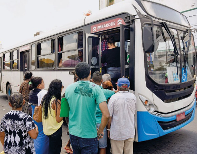 Imagem: Fotografia. Pessoas enfileiradas ao lado de um ônibus com a porta aberta.   Fim da imagem.