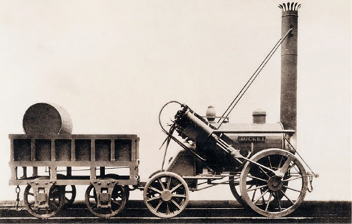 Imagem: Fotografia em preto e branco. Uma locomotiva com uma chaminé alta na frente e um vagão na parte de trás.   Fim da imagem.