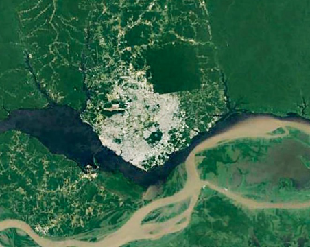 Imagem: Fotografia de satélite. No centro há um rio sinuoso e em volta, terras verde-escuro com manchas brancas e um caminho marrom.  Fim da imagem.