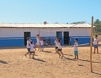 Imagem: Fotografia. Campo de areia com crianças jogando vôlei. Fim da imagem.