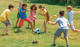 Imagem: Fotografia. Quatro meninos e três meninas jogam bola de futebol em um campo. Fim da imagem.