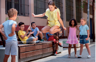 Imagem: Fotografia. Meninos e meninas sobre uma rua pulando corda. Fim da imagem.