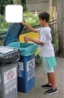 Imagem: Fotografia. Menino de cabelo curto preto cacheado, vestindo camiseta branca e bermuda verde. Ele joga uma lata de refrigerante em uma lixeira azul indicando “recicláveis”, ao lado, uma lixeira cinza indicando “não recicláveis”. Fim da imagem.