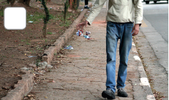 Imagem: Fotografia. Destaque de tronco, braços e pernas de um homem andando em uma calçada. Ele joga papéis no chão. Fim da imagem.