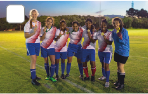 Imagem: Fotografia. Sete meninas de uniforme de camiseta branca e bermuda azul, estão abraçadas, segurando medalhas douradas. Fim da imagem.