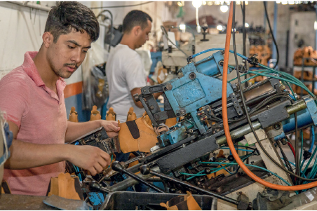 Imagem: Fotografia. Homens em maquinários com sapatos ligados a máquinas altas de plataformas com alavancas, fios e botões ligados ao meio produtivo. Fim da imagem.