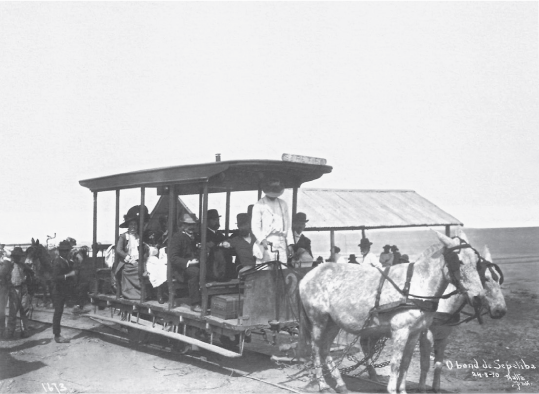 Imagem: Fotografia em preto e branco. Bonde com seis fileiras de acentos puxada por dois cavalos.  Fim da imagem.