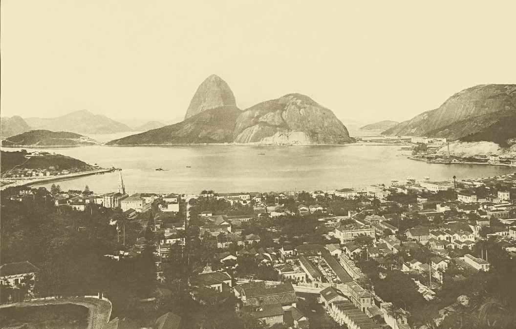 Imagem: Fotografia antiga. Ao centro, uma montanha com o Pão de Açúcar. Ao redor, már. E em frente, uma cidade. Fim da imagem.