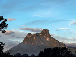 Imagem: Fotografia. Vista de uma montanha cercada por vegetação. Há neblina por todo o seu arredor. Fim da imagem.