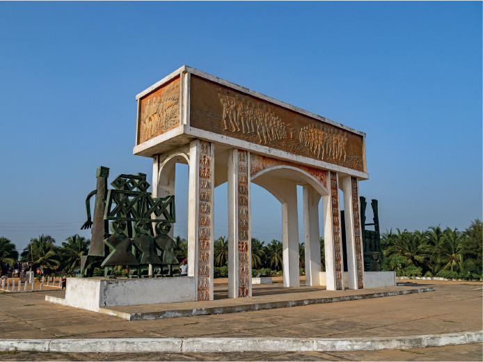 Imagem: Fotografia. Monumento retangular horizontal com alto-relevo de homens enfileirados com árvore no centro. Abaixo, há colunas retangulares verticais formando arcos no interior com escultura de homens por toda a coluna. Fim da imagem.