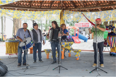 Imagem: Fotografia. Homens em um coreto tocando instrumentos musicais. Fim da imagem.