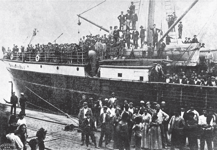 Imagem: Fotografia em preto e branco. Navio repleto de pessoas sobre parte aberta observando multidão de pessoas em frente ao navio no porto. Fim da imagem.
