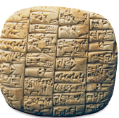 Imagem: Fotografia. Escultura retangular com pontas arredondadas, há muitas divisões com inscrições em símbolos cuneiformes.   Fim da imagem.