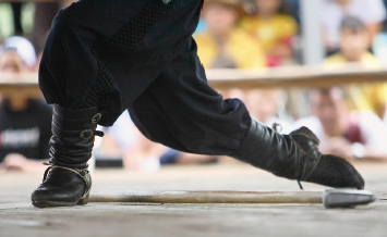 Imagem: Fotografia. Destaque para as pernas de uma pessoa, está de calça e bota preta. Uma perna está dobrada à frente e outra esticada para trás.  Fim da imagem.