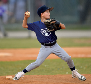 Imagem: Fotografia. Um menino usando chapéu e camiseta azul, está com a mão direita flexionada para trás e segura uma bola branca, na mão esquerda usa uma luva.  Fim da imagem.