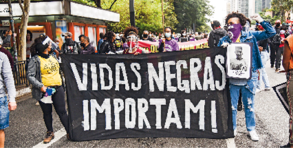 Fotografia. Pessoas segurando uma faixa com a informação: VIDAS NEGRAS IMPORTAM! Ao fundo, árvores e prédios.