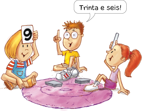 Ilustração. A menina loira segura uma carta com o número 9 na testa. Na frente dela, a menina ruiva segura outra carta na testa. Entre elas, o menino diz: Trinta e seis!