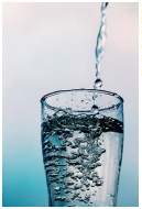 Imagem: Fotografia. Um copo cheio de água, com água caindo dentro do copo, formando bolhas.  Fim da imagem.
