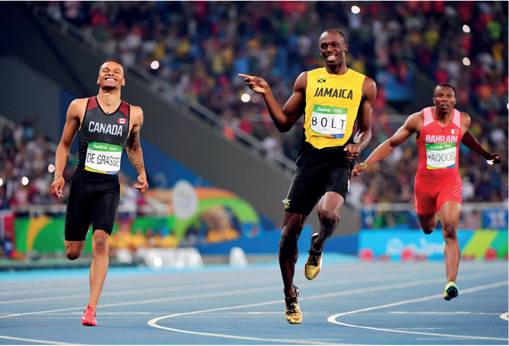 Imagem: Fotografia em Página dupla. À esquerda, um homem com regata, estampado o nome: CANADA, e short. Ele corre e sorri. Ao lado, outro homem, nego usando uma regata, com estampa: JAMAICA e short. Ele aponta com o dedo indicador da mão esquerda para o lado e sorrindo. Atrás, um homem correndo.  Fim da imagem.