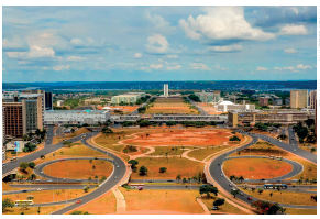 Imagem: Fotografia. Vista aérea de um rodoanel ao redor há prédios.  Fim da imagem.