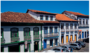 Imagem: Fotografia. Casas de dois andares com portas e janelas e telhado padrões.  Fim da imagem.