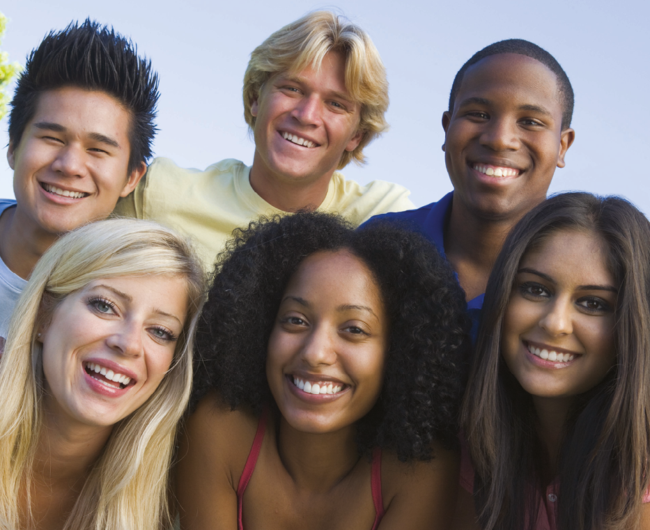 Fotografia. Seis jovens sorrindo. Na fileira de trás: rapaz asiático de cabelo preto com um topete; rapaz branco de cabelo loiro liso e camiseta amarela; rapaz negro de cabelo raspado e camiseta azul. Na fileira da frente: moça loira de cabelo liso longo; moça negra de cabelo cacheado preto na altura dos ombros e camiseta regata rosa; moça branca de cabelo liso longo e castanho.