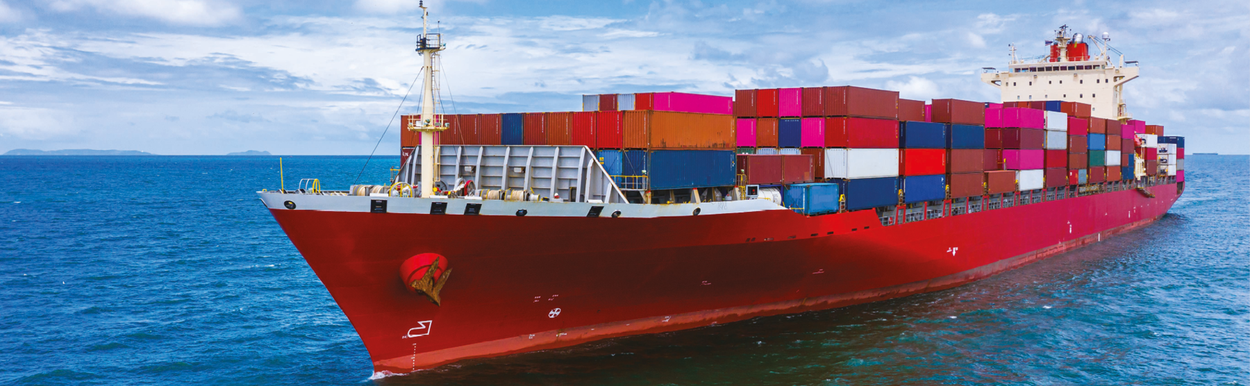 Fotografia. Um navio no mar, com o casco vermelho e contêineres coloridos empilhados em cima.