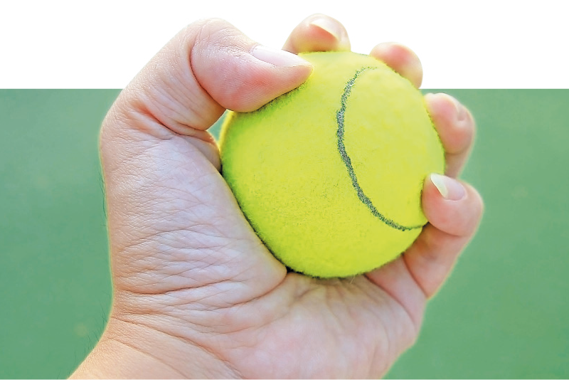 Fotografia. Destaque para a mão de uma pessoa segurando uma bola de tênis.