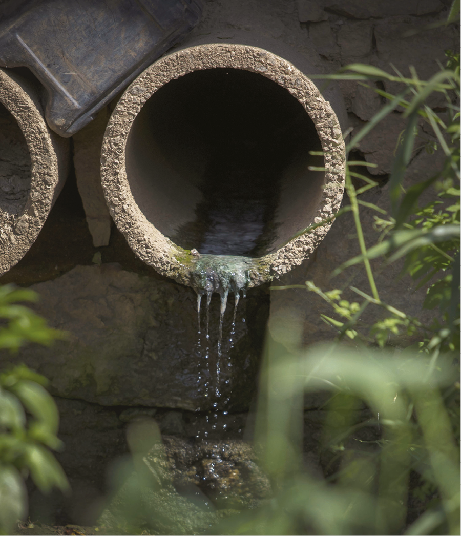 Fotografia. Um grande tubo de concreto, do qual escorre água escura.