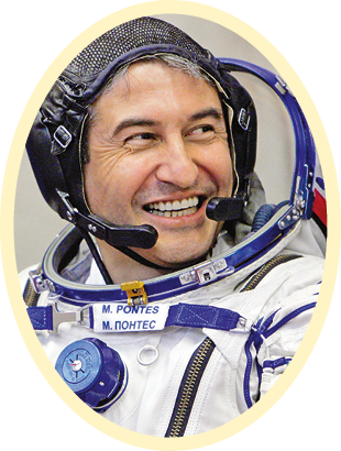 Fotografia de um homem com roupa de astronauta, ainda sem capacete, com intercomunicador. Ele está sorrindo.