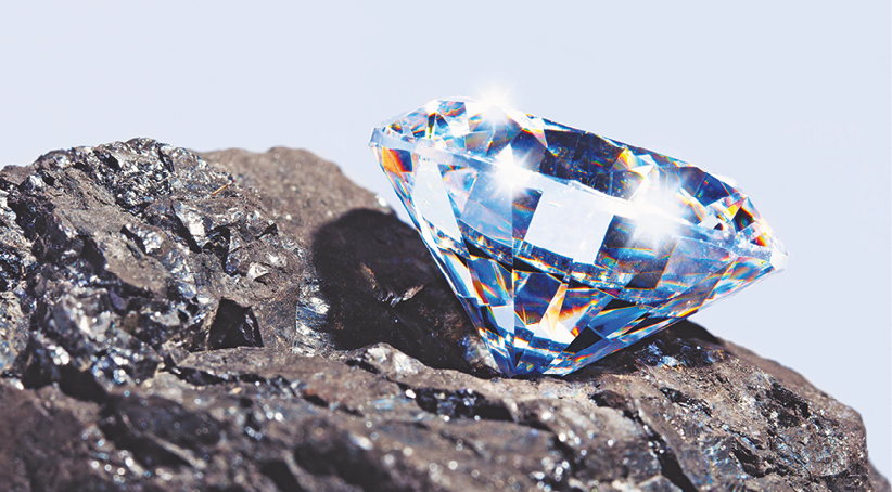 Fotografia. Um diamante em cima de uma rocha cinza-escura.
