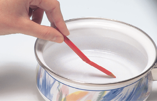 Fotografia. Uma pessoa segurando um lápis vermelho dentro de um recipiente com água. A parte do lápis que está submersa parece torta.