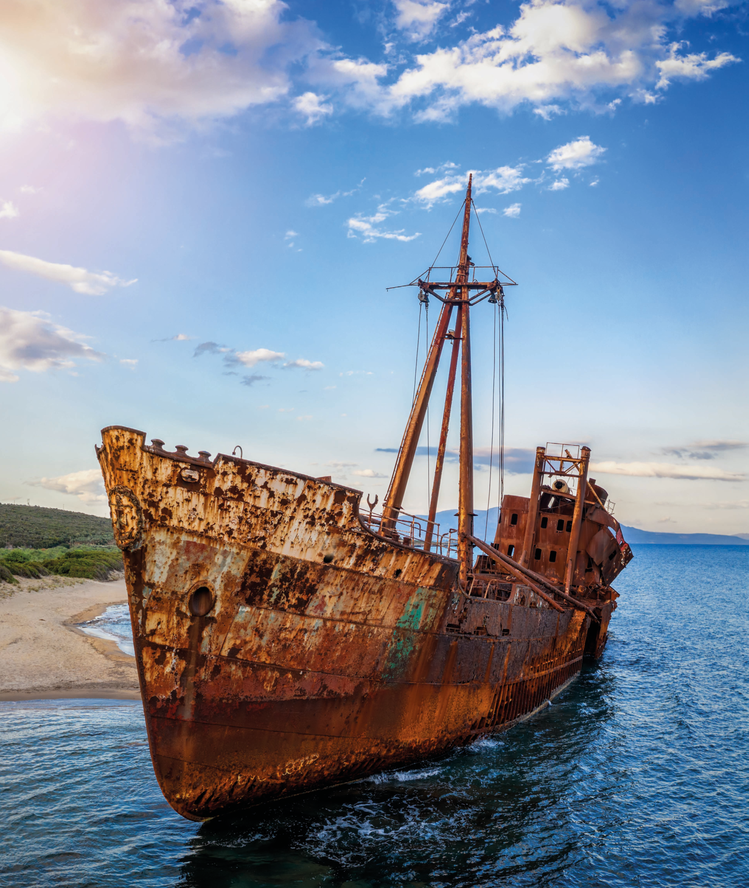 Fotografia. Um navio no mar, próximo a uma praia. O navio está todo enferrujado.