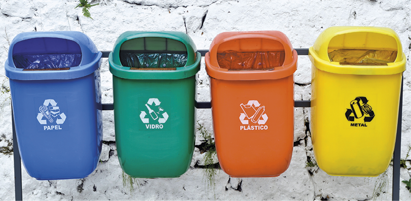 Foto. 4 cestos para coleta de lixo recicláveis, um ao lado do outro. Da esquerda para a direita: azul, verde, laranja e amarelo.